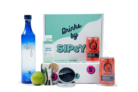 A collection of cocktail making supplies from Sipsy, including bottles of tequila and limeade, simple syrup, a shaker, ice tongs, and a recipe card, all displayed in front of a white background.