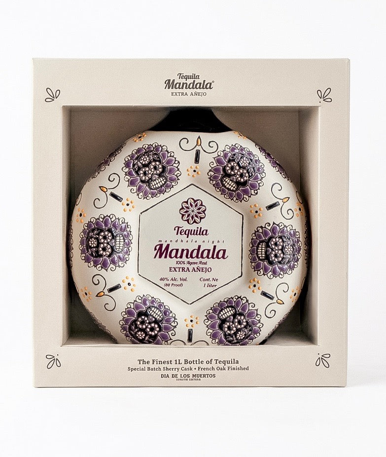 A boxed bottle of Tequila Mandala Extra Agrio tequila, shown in its cream-colored retail packaging with a clear window revealing the round bottle decorated with purple mandala patterns.